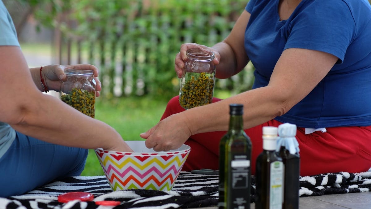 Two people preparing herbs in jars outdoors with fresh ingredients and oils.